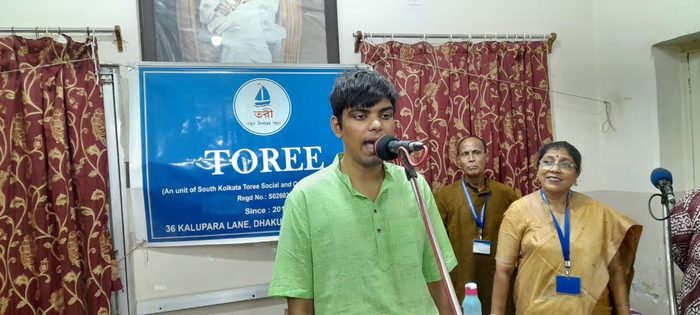 A young man singing at a microphone in front of the TOREE banner.
