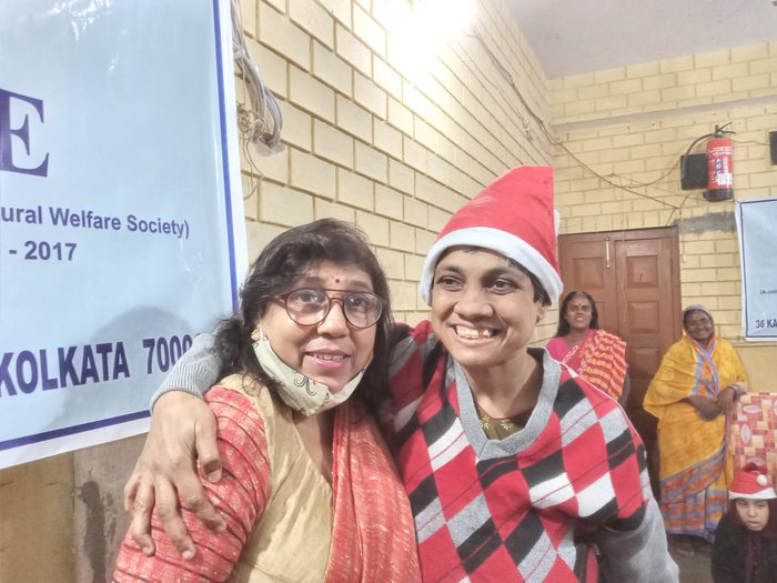 Two women in Santa hats smiling together, one with her arm around the other.