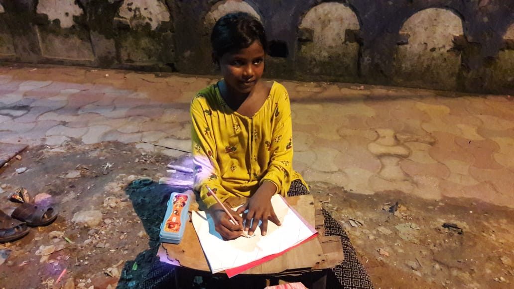 A girl drawing on a sheet of paper on the pavement.