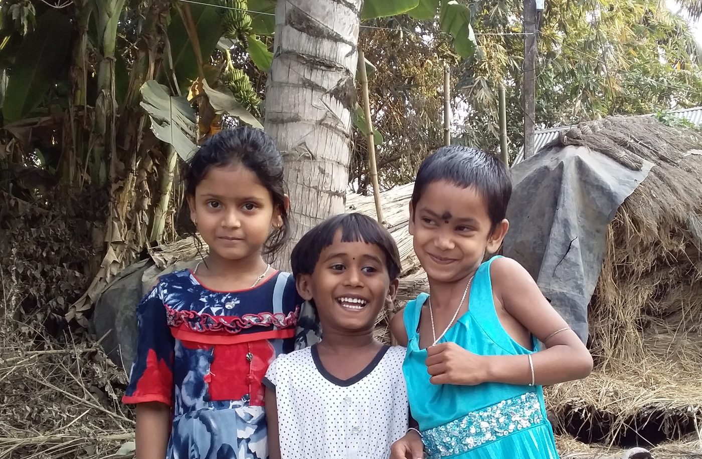 Three children outside their home in a village where TOREE distributes garments and mosquito nets.