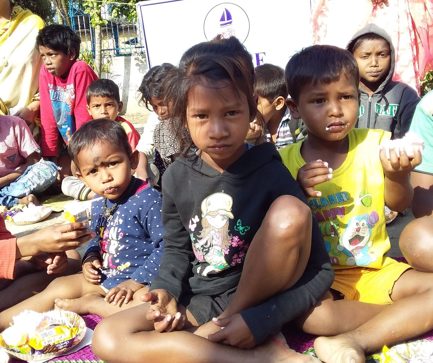 Children sitting together with plates of food at a street celebration.