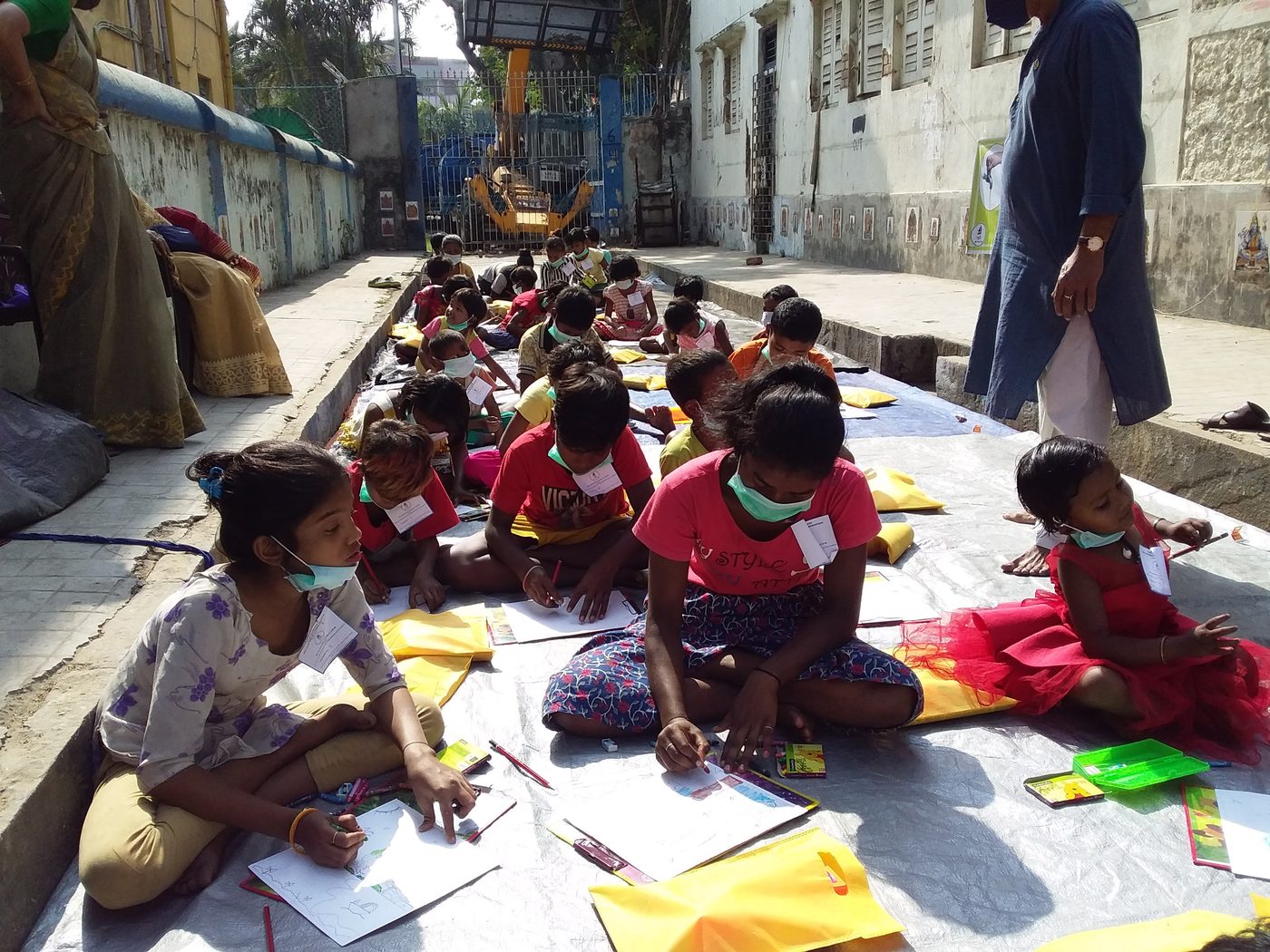 Children in masks drawing on sheets spread along a Kolkata street.
