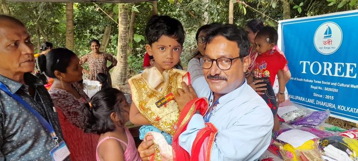 A member of TOREE holding up a new garment for a small child beside the TOREE banner.