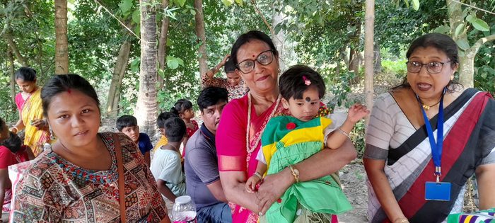 Members of TOREE with a small girl in a new dress at a village camp, October 2025.