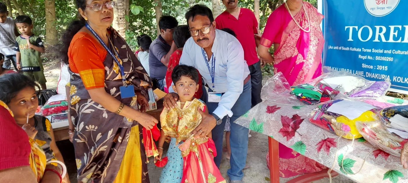 Members of TOREE helping a small girl into a new dress beside the TOREE banner at a village camp.