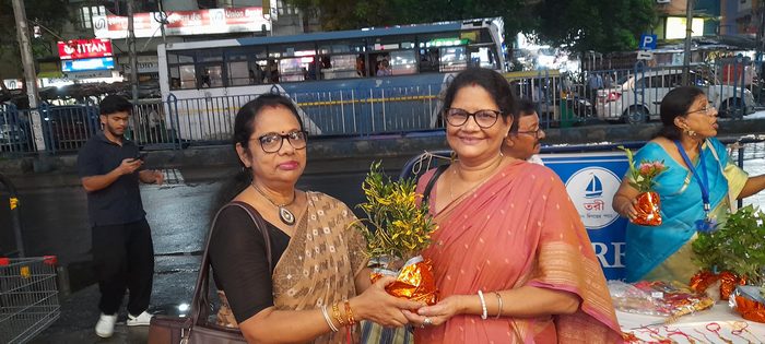 Two members of TOREE holding a potted plant at the Rakhi Bandhan stall on a Kolkata street, August 2026.