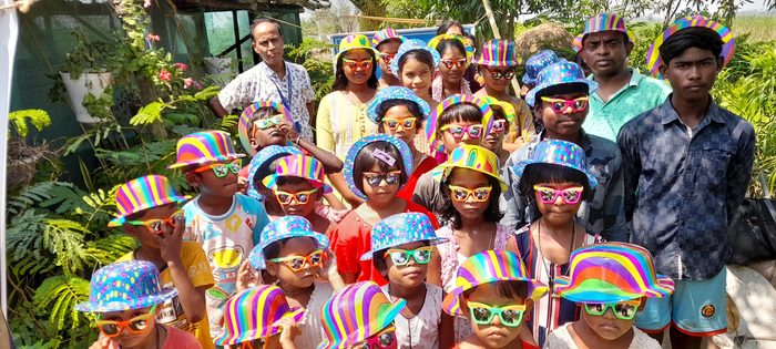 A large group of village children in party hats and sunglasses at the Holi celebration.