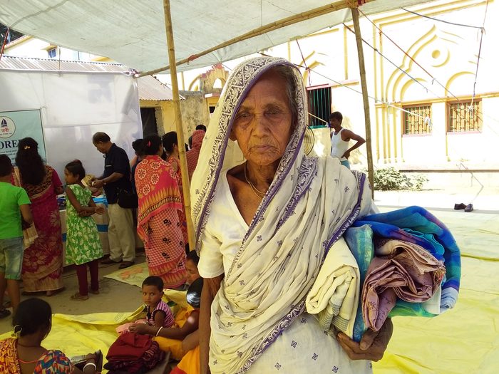 An elderly woman holding a blanket at a village distribution camp.