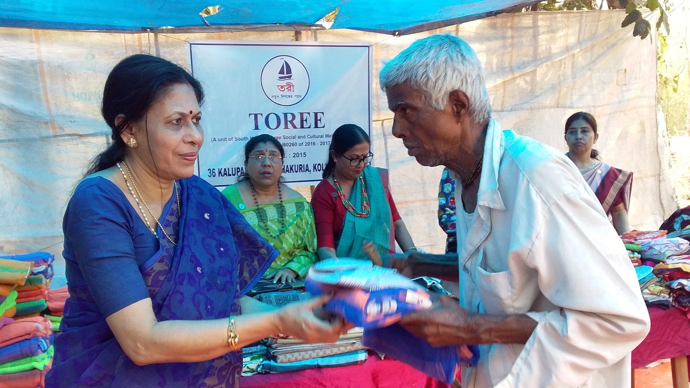 Volunteers handing out folded garments from tables at a village camp.