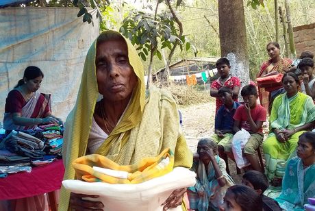 An elderly woman holding garments received at a village distribution camp.