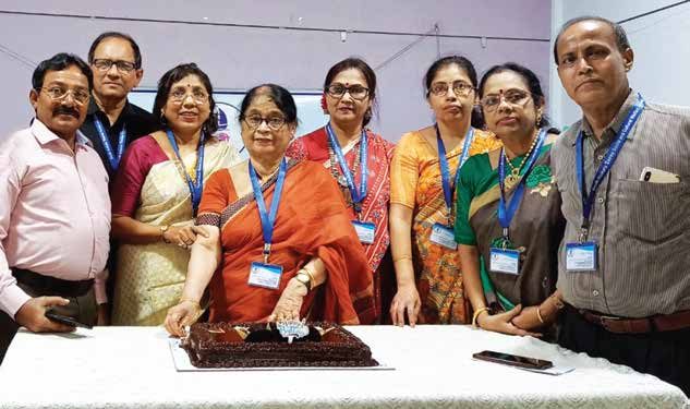 Eight members of TOREE standing behind a table as a cake is cut.