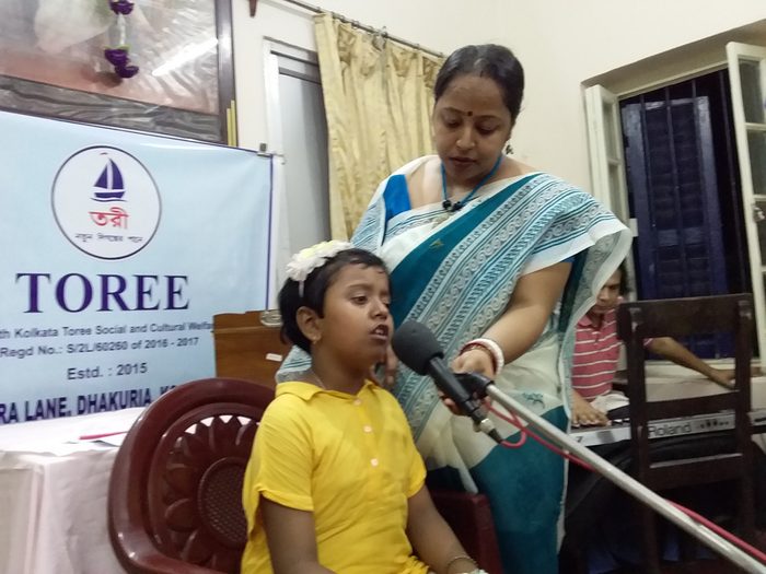 A young child singing at a microphone, supported by a member of TOREE.