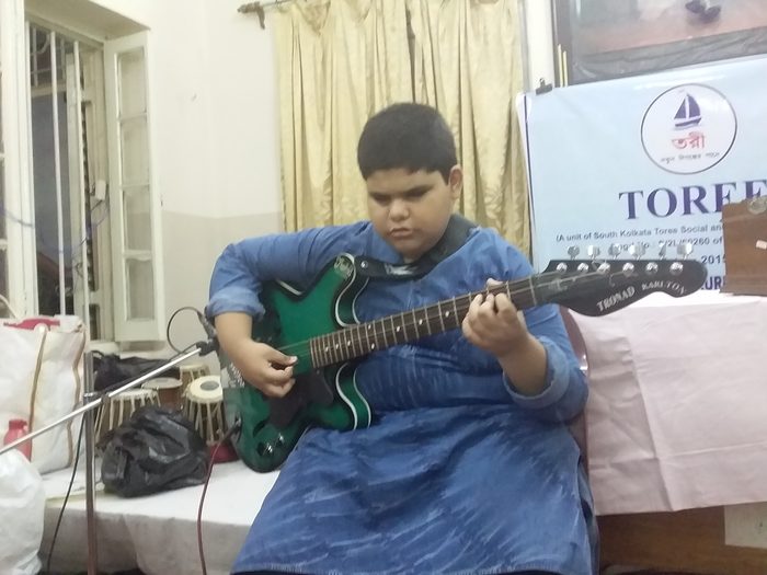 A boy playing an electric guitar at a club programme.