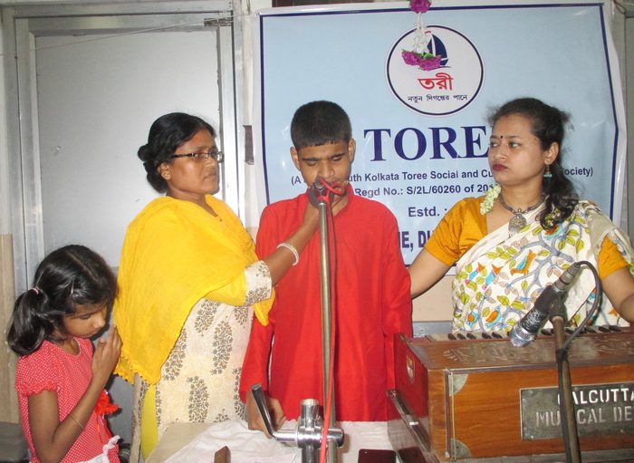 A student singing at a Kobi Pranam programme, accompanied by members.