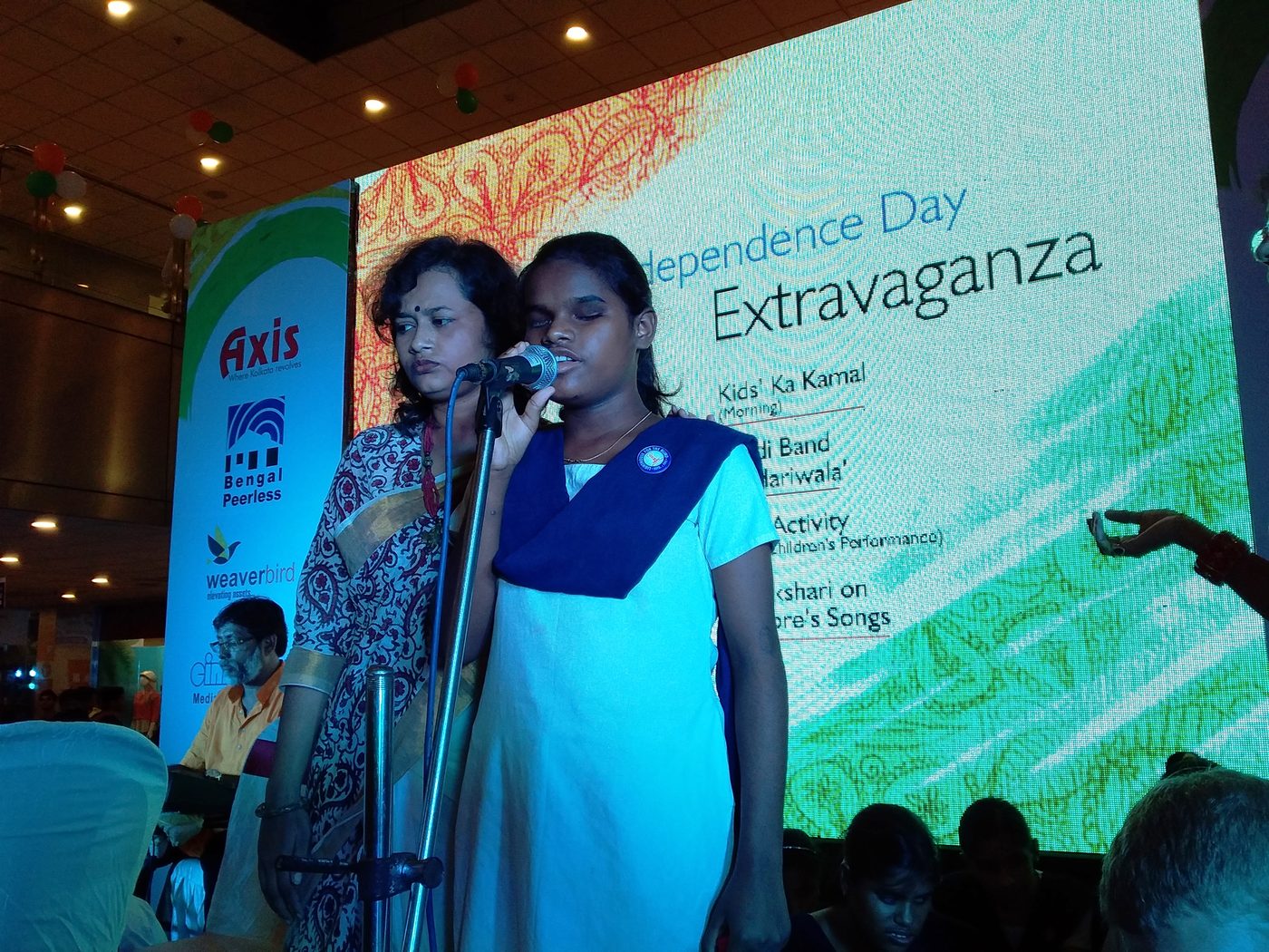 Two visually impaired students singing into microphones on a brightly lit stage.